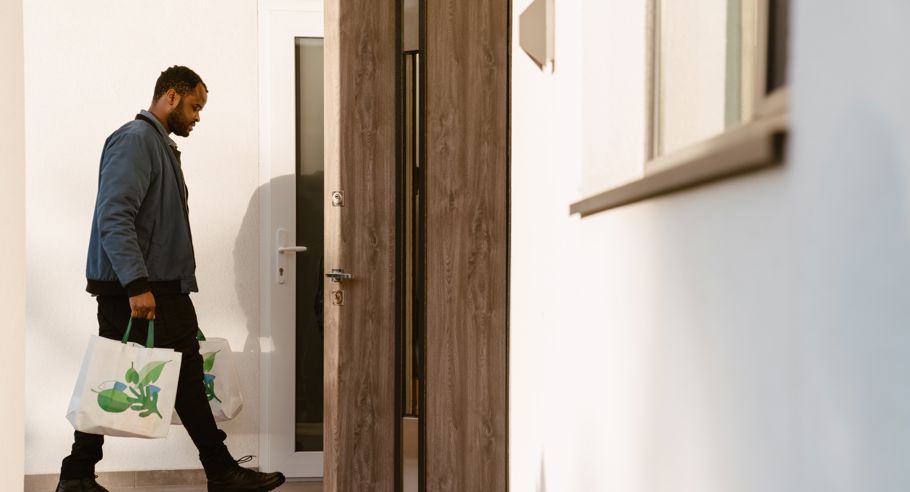 A man holding groceries walking through a door